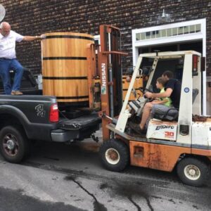 a man and his son driving a fork lift and moving a barrel from the back of a truck