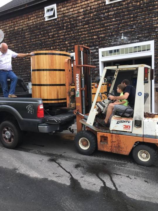a man and his son driving a fork lift and moving a barrel from the back of a truck