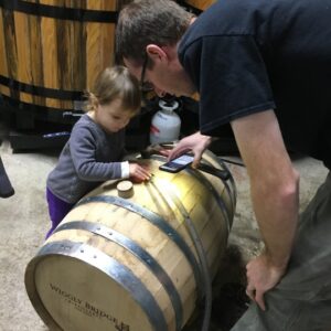 a man in a black shirt holding an iphone, using it as a flashlight while showing a little girl something on a barrel