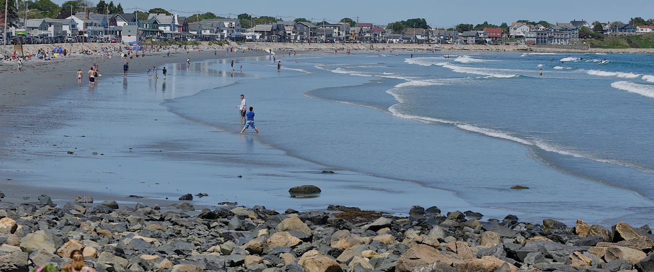 A scenic beach with people strolling on the shore, with a kite soaring in the sky.