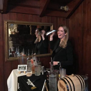 a woman behind a booth shaking a drink shaker and posing for a photo