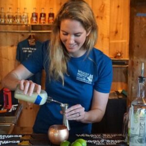 a woman with blonde hair and a blue short sleeve shirt making a cocktail