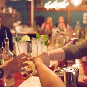 3 people sitting at a bar cheersing their drinks