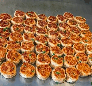 a spread of crab cakes on a table, light topped with green garnish on top