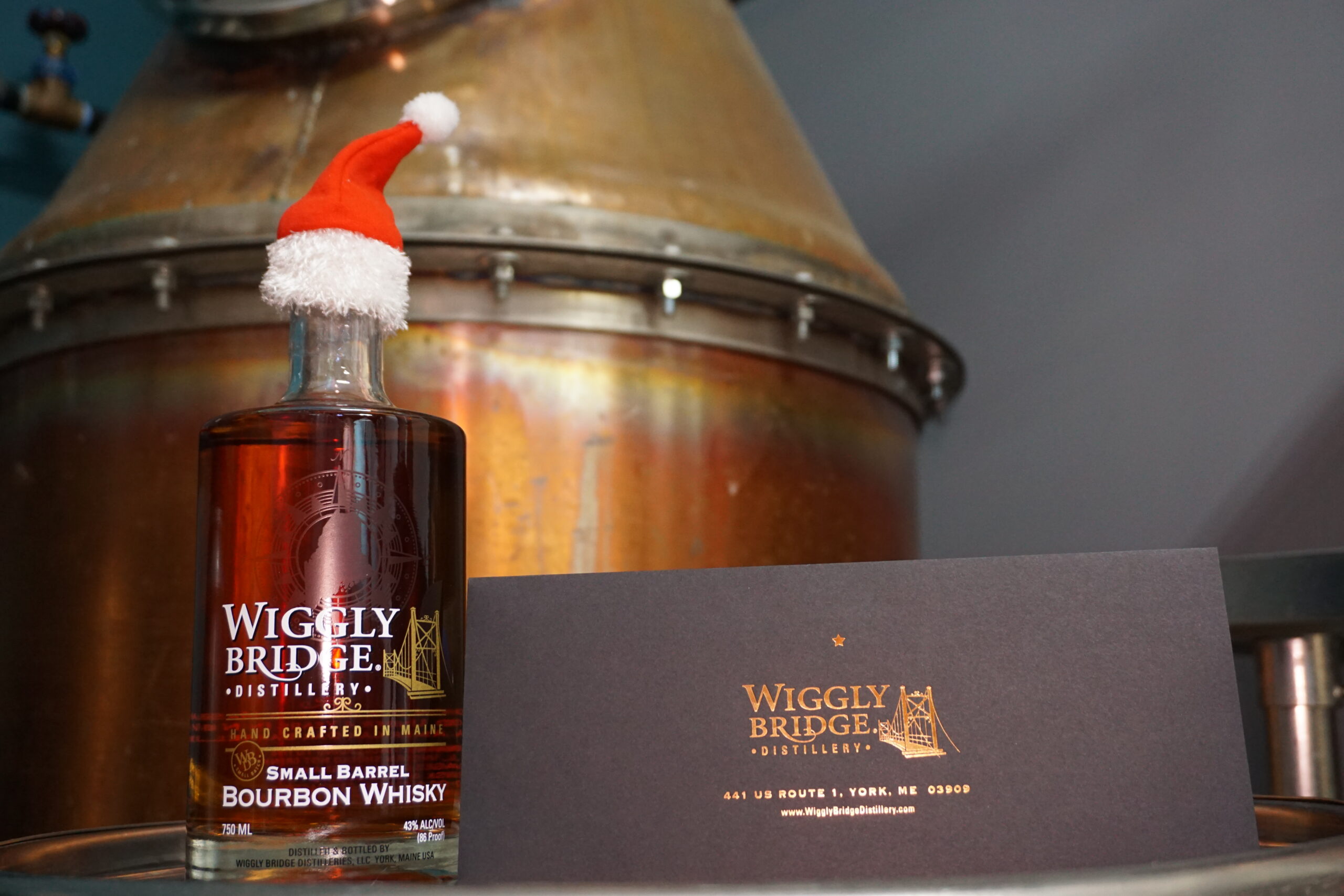 a bottle of wiggly bridge bourbon whiskey wearing a little santa hat next to a gift certificate