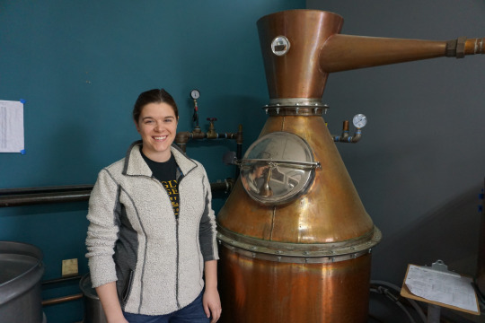 a woman with her hair pulled back and a zip up sweatshirt at a distillery
