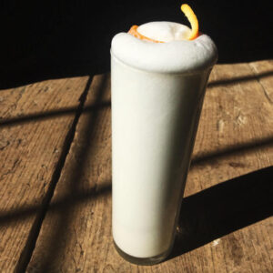 a white drink in a tall cocktail glass with an orange peel garnish on top