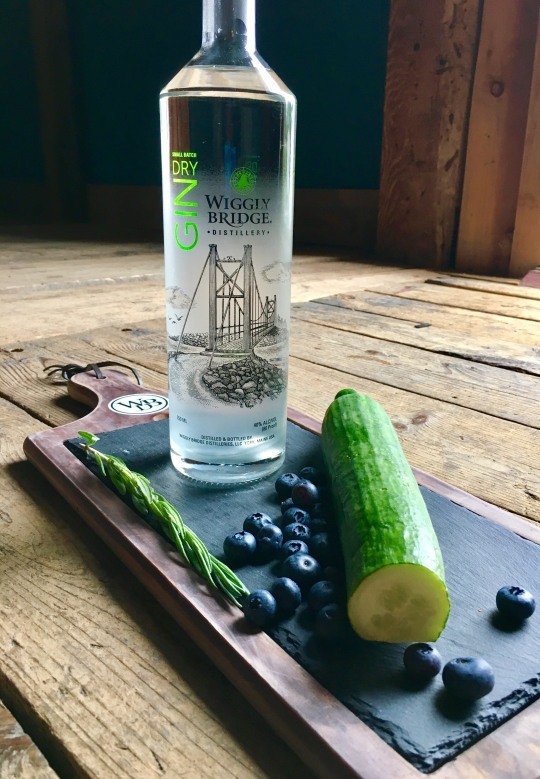 a gin bottle, surrounded by blueberries and cucumbers